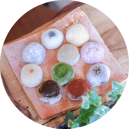 Mochis multicolores sur une planche en bois rustique, chacun montrant une texture unique. Ces douceurs sont fabriquées sans gluten et sont entièrement végétales, reflétant le savoir-faire artisanal de Lacigne.